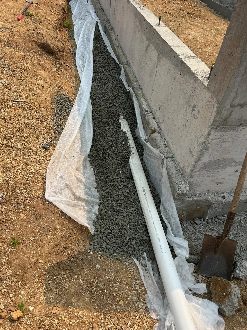 Drainage pipe, gravel, and fabric alongside a concrete foundation