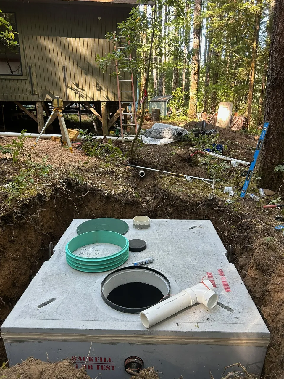 Concrete septic tank with a green access riser beside a woodland home